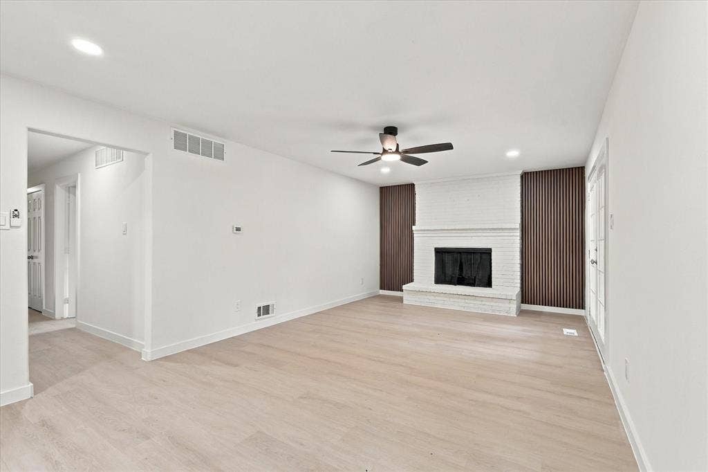 Interior space featuring wood-finish flooring, a painted brick fireplace with hearth, vertical wood-slat accent wall panels, a ceiling fan with integrated lighting, and recessed ceiling lights
