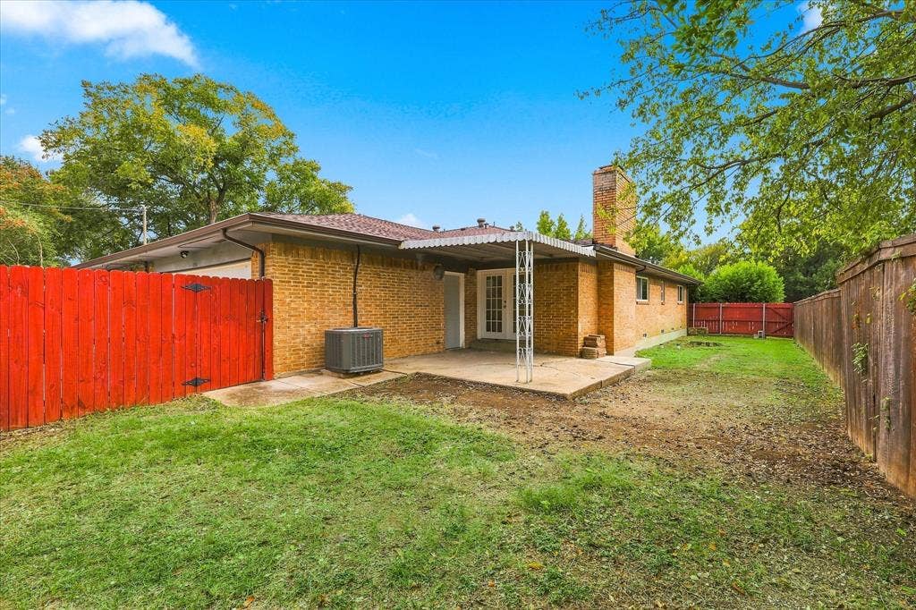 Brick exterior residence featuring a covered concrete patio, masonry chimney, and fenced backyard