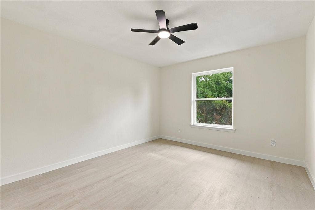 Neutral-toned interior space featuring wood-finish flooring, a single-hung window, and a five-blade ceiling fan with integrated lighting