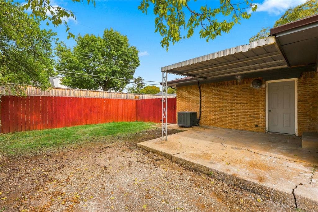 Brick exterior, covered concrete patio, and fenced backyard with established trees