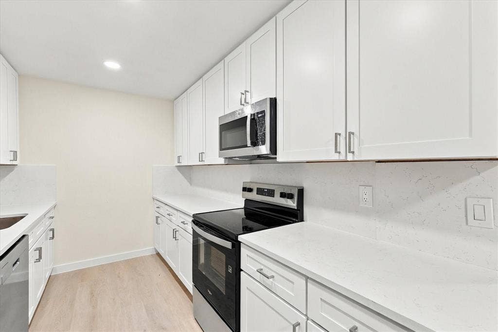Kitchen featuring white shaker-style cabinetry, solid-surface countertops, matching slab backsplash, stainless steel appliances, and wood-finish flooring
