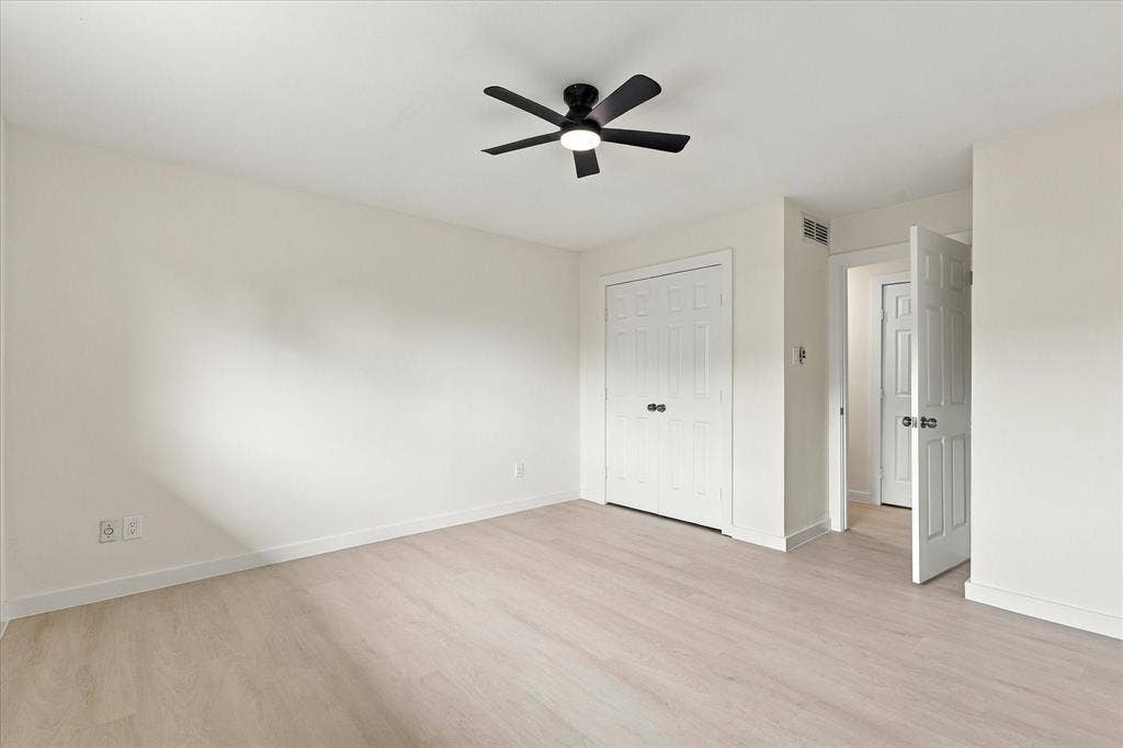 Neutral interior space featuring wood-finish flooring, a matte black ceiling fan with integrated lighting, and white six-panel doors