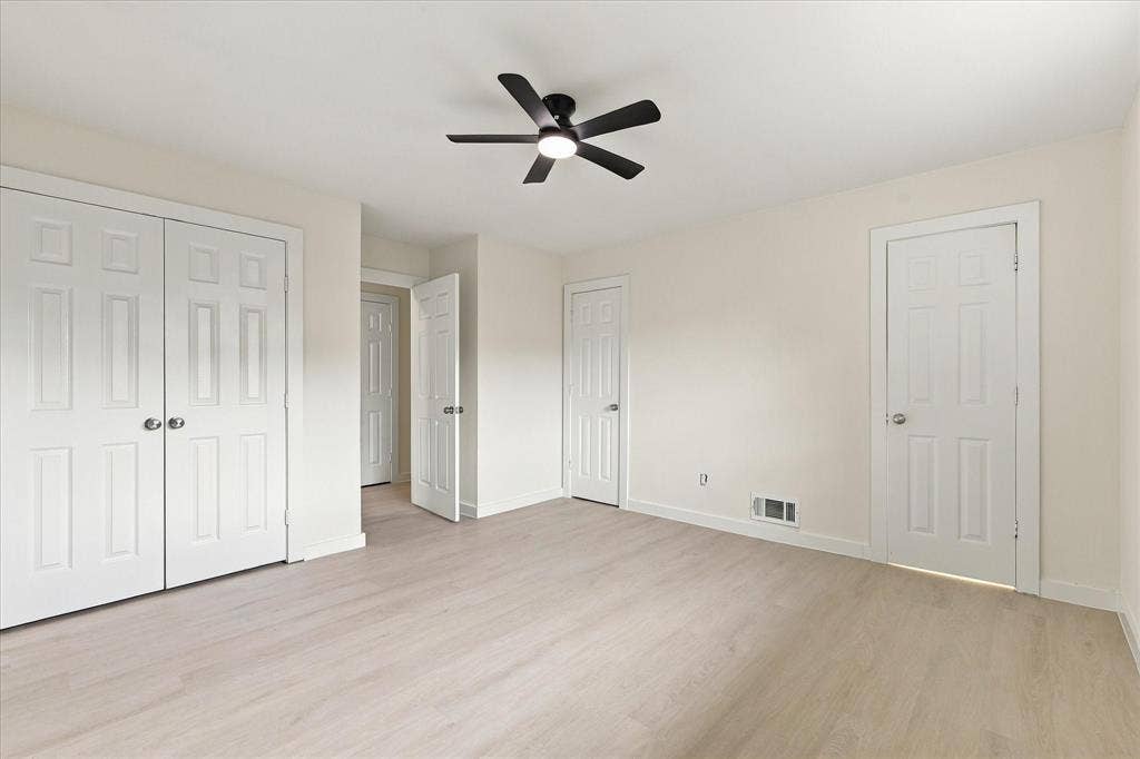 Room featuring wood-finish flooring, a central ceiling fan with integrated lighting, and multiple six-panel interior doors