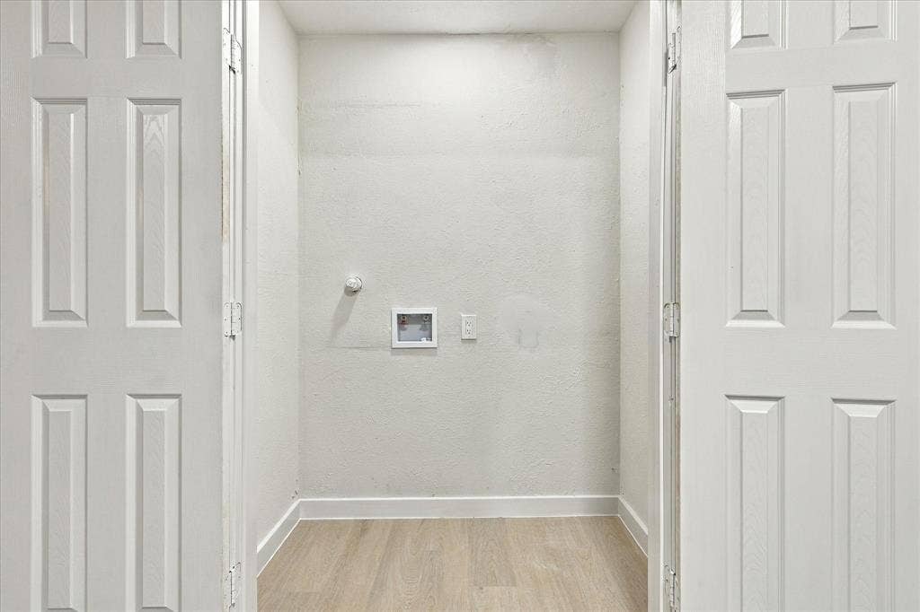 Dedicated utility alcove featuring dual-panel closet doors, wood-finish flooring, and recessed laundry hookups