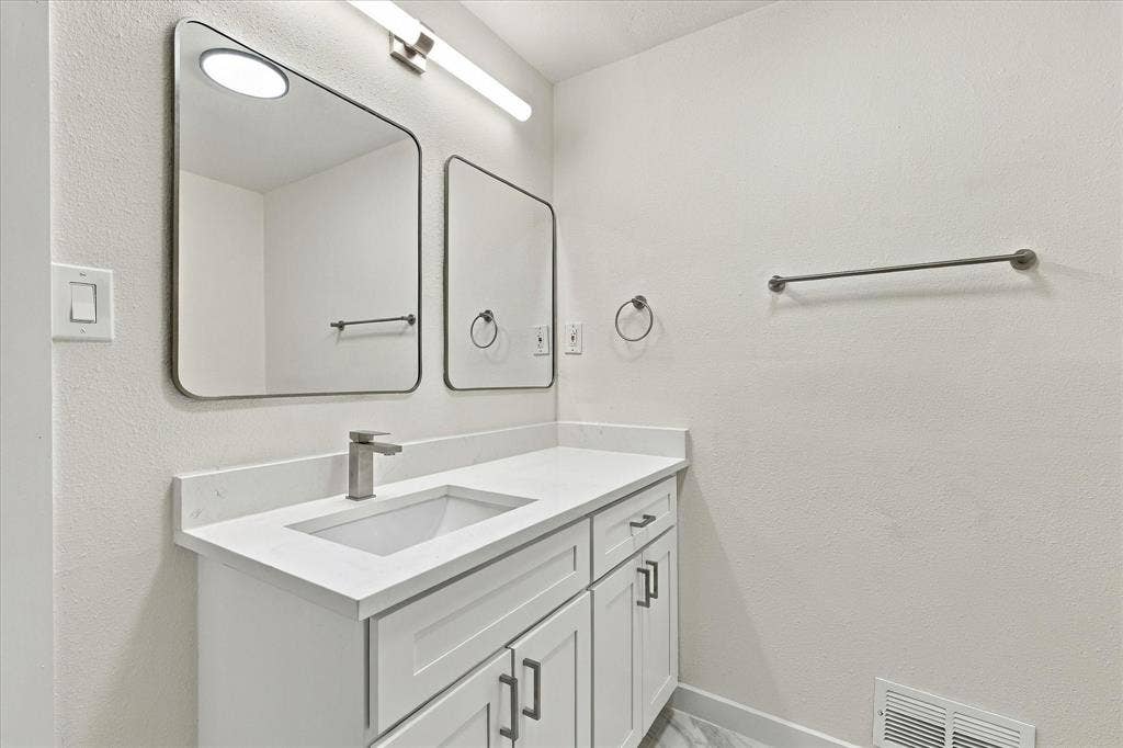White vanity featuring a solid surface countertop, rectangular under-mount sink, brushed-nickel hardware, dual wall-mounted mirrors, and linear overhead lighting