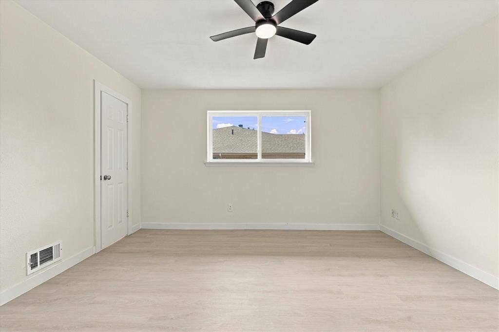 Neutral interior space featuring wood-finish flooring, a matte black ceiling fan with integrated lighting, and a single-hung window with white trim