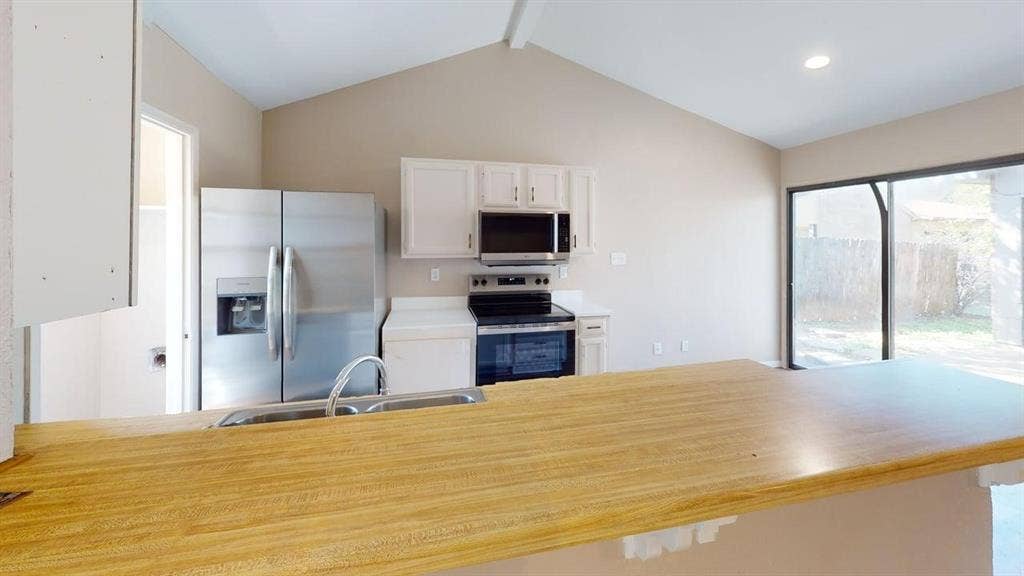 510 Matterhorn Street, Cedar Hill, TX 75104 Kitchen featuring a vaulted ceiling, wood-finish breakfast bar, stainless steel appliances, white cabinetry, and sliding glass doors