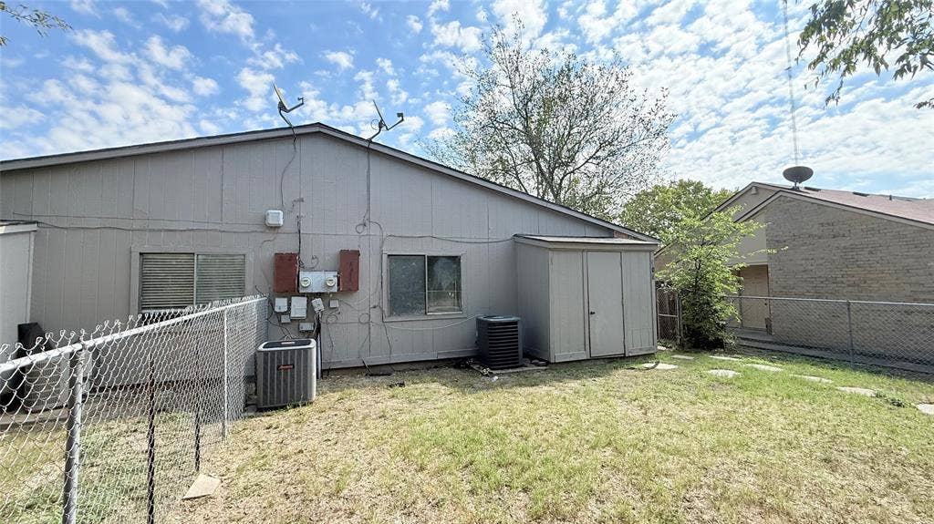 510 Matterhorn Street, Cedar Hill, TX 75104 Exterior elevation featuring vertical panel siding, metal chain-link fencing, built-in outdoor storage shed, and external HVAC units
