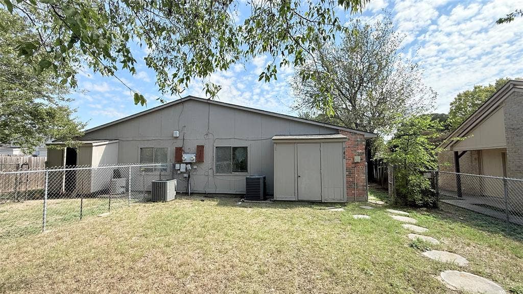 510 Matterhorn Street, Cedar Hill, TX 75104 Rear exterior featuring vertical siding, brick accents, integrated storage structures, and a chain-link fenced yard with a stone path