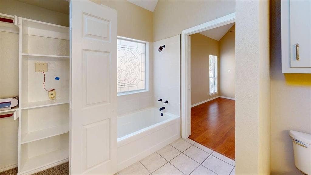 Bathroom featuring a soaking tub, matte black fixtures, custom decorative window pane, built-in shelving, and tile flooring