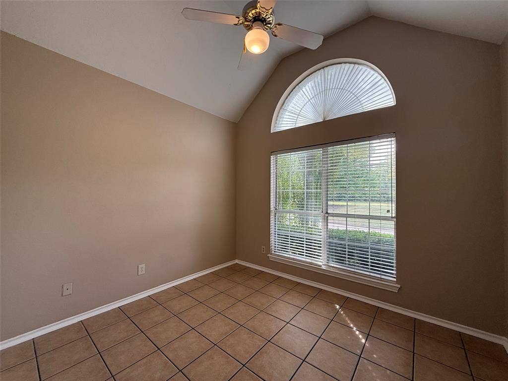 Vaulted ceilings, arched window featuring a sunburst design, tile flooring, and a ceiling fan with integrated lighting