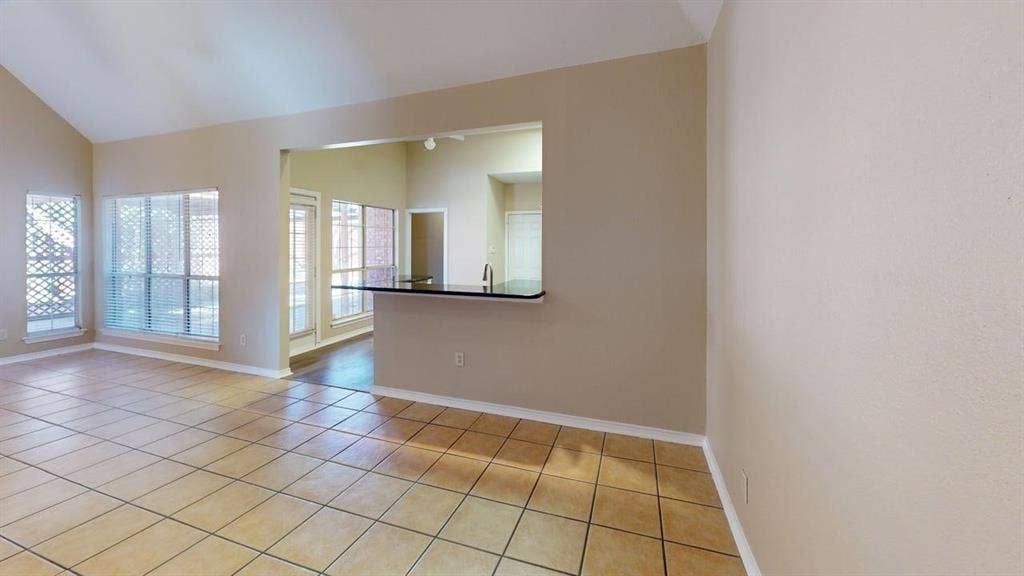 Vaulted ceilings, neutral wall tones, large windows, ceramic tile flooring, and a breakfast bar with a solid surface countertop