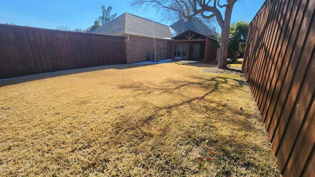 Backyard featuring a brick exterior, covered patio, wood privacy fencing, and a mature tree