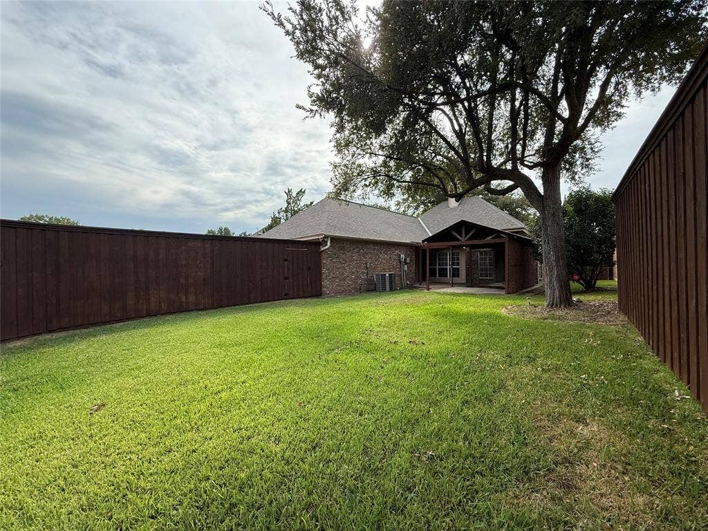 Backyard featuring a grass lawn, mature trees, wood privacy fencing, and a covered patio area