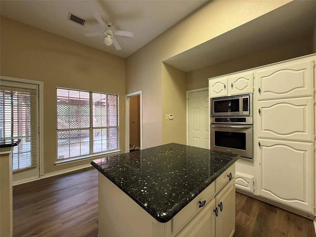 Kitchen area featuring a central island with a dark stone countertop, built-in stainless steel double wall ovens, white cabinetry, wood-finish flooring, and a vaulted ceiling