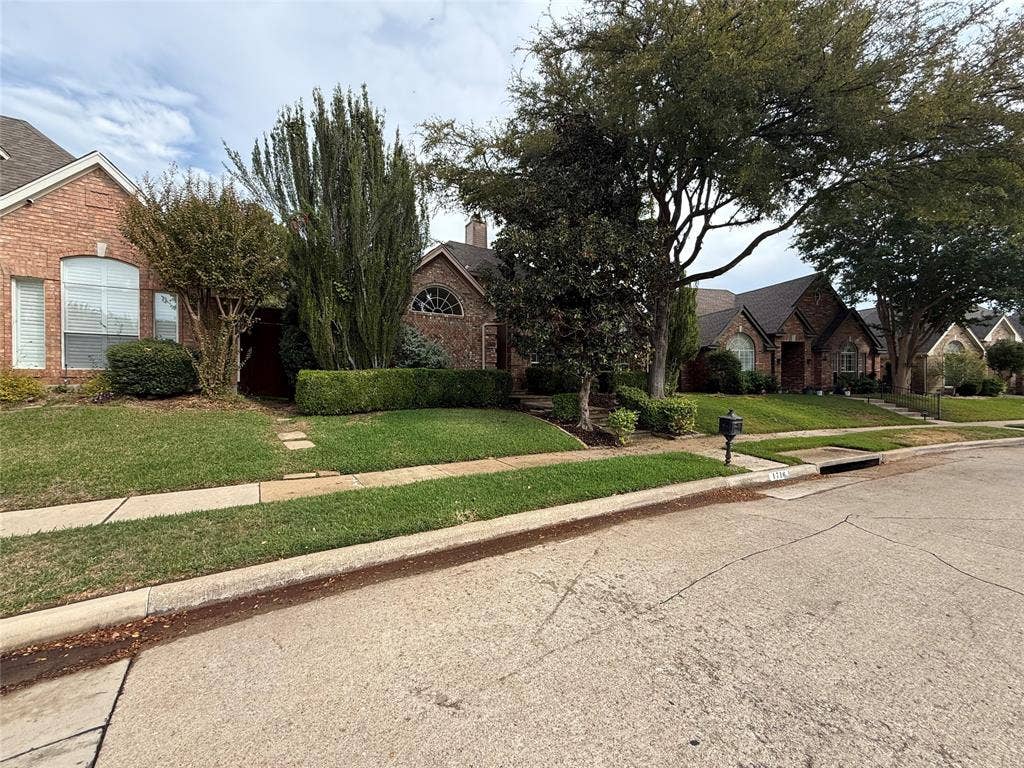 Brick exterior, arched window detailing, and mature landscaping featuring manicured hedges and trees
