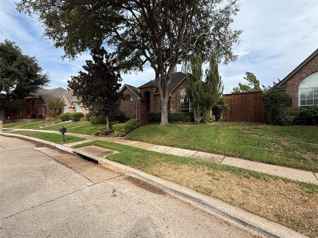 Brick exterior facade with arched window detailing, mature shade trees, and a wood privacy fence