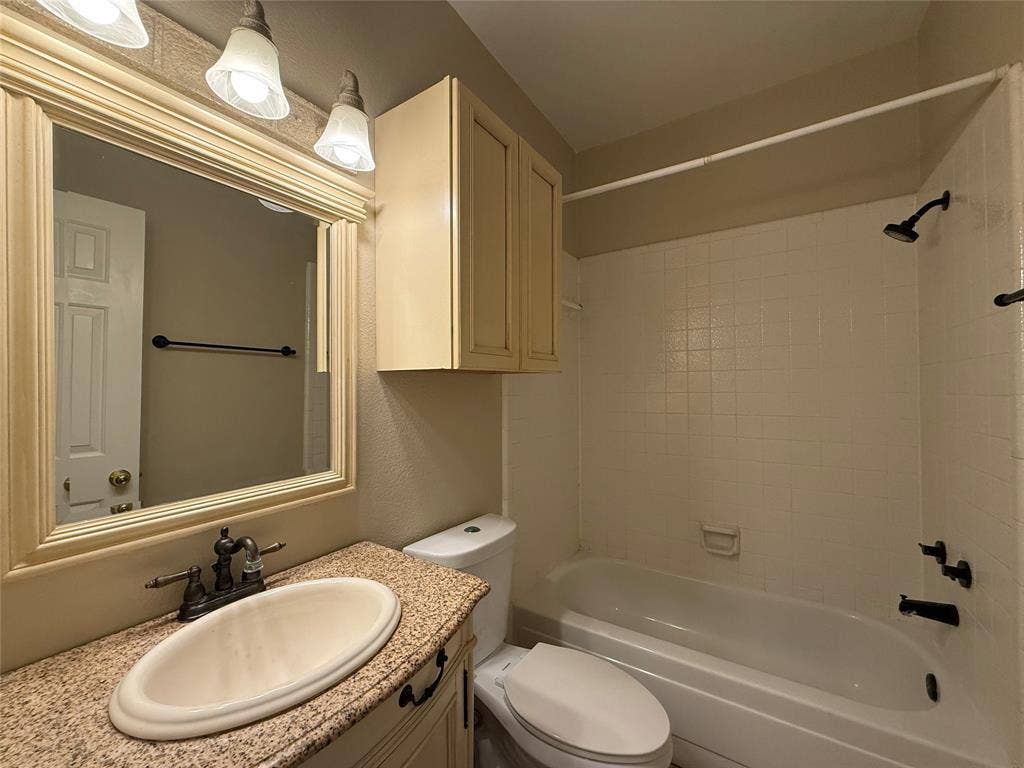 Bathroom featuring a vanity with a speckled countertop, oval undermount sink, three-light fixture, built-in cabinetry, and a shower-tub combination with tiled surround