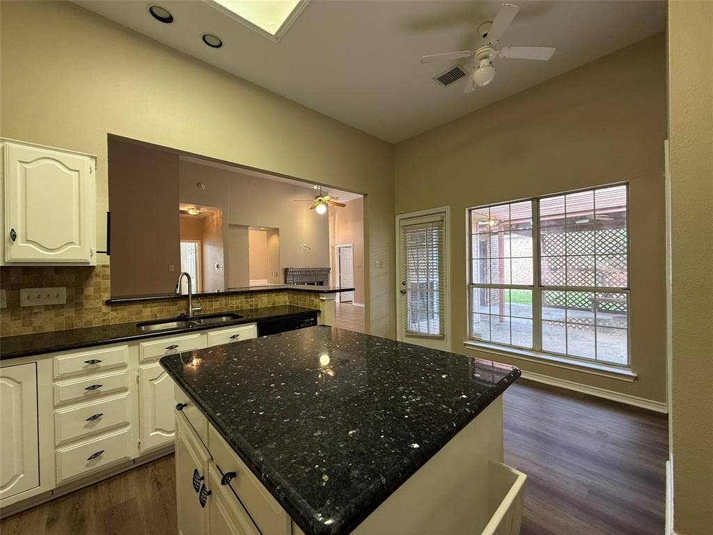 Kitchen featuring a center island with dark stone countertops, custom white cabinetry, recessed ceiling lighting, wood-finish flooring, and large windows