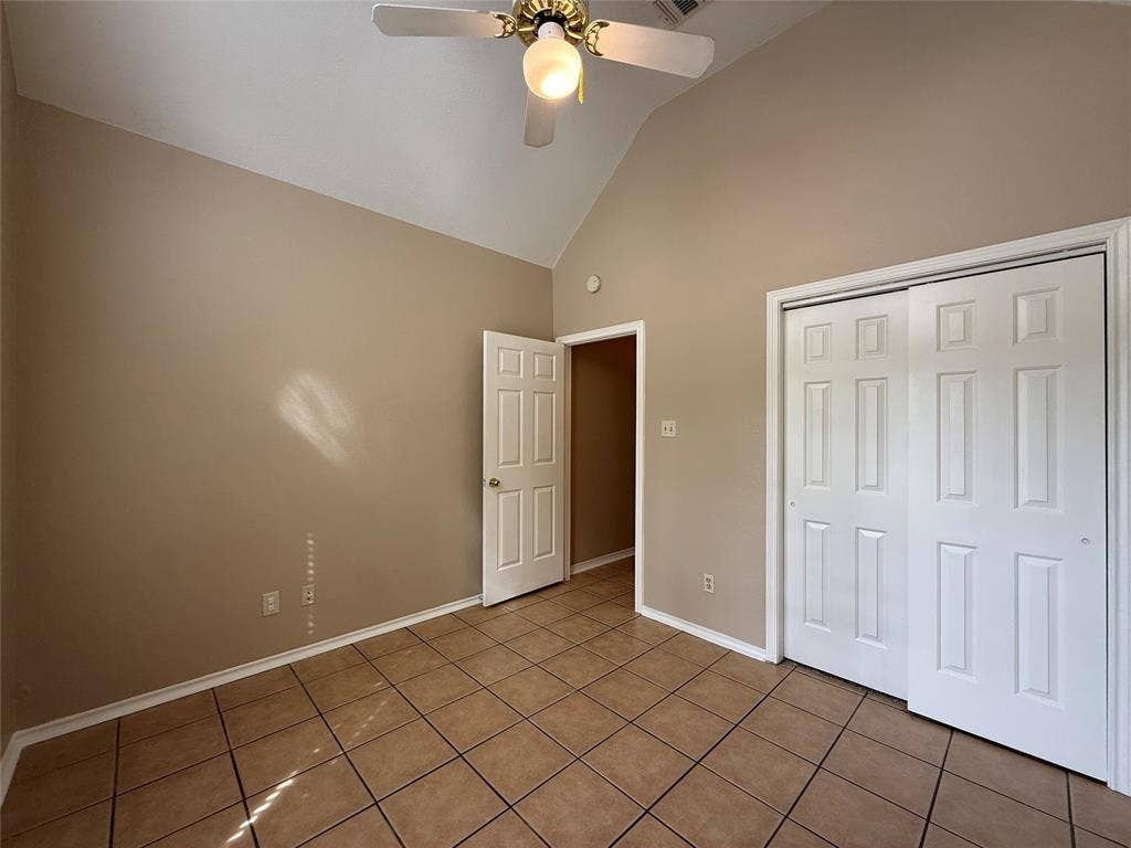 Vaulted ceiling with a centrally mounted ceiling fan, ceramic tile flooring, and a multi-panel sliding closet door