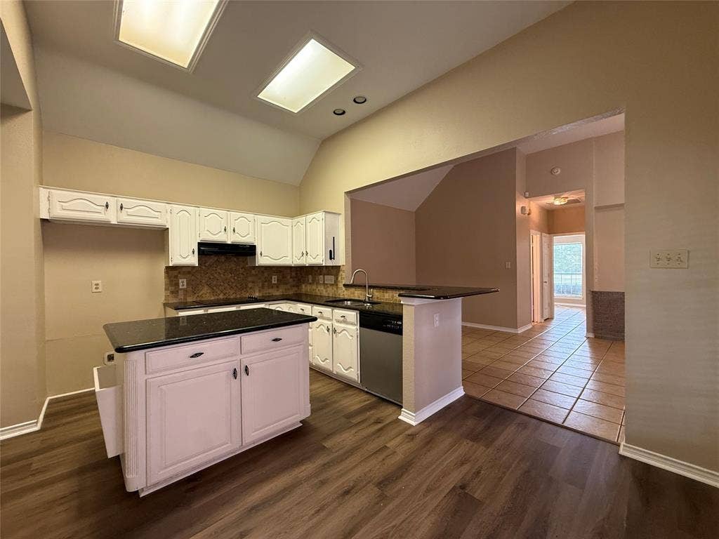 Kitchen featuring white cabinetry, dark stone countertops, a center island, stainless steel dishwasher, and wood-finish flooring