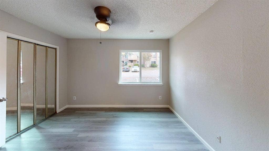 Interior room featuring wood-finish flooring, sliding mirrored closet doors, a ceiling-mounted light fixture, and a window with a white frame