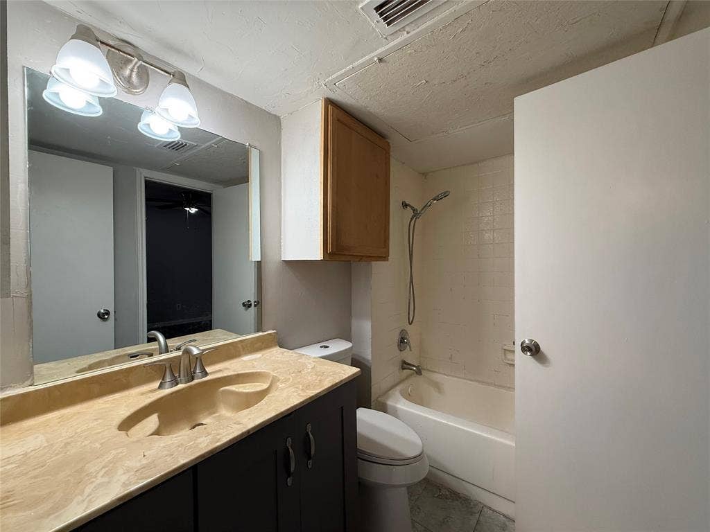Bathroom featuring a stone-composite countertop with an integrated sink, dark wood-finish vanity cabinetry, wall-mounted medicine cabinet, and a shower-tub combination with tiled surround