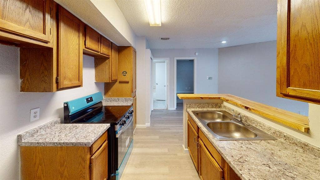 Kitchen featuring wooden cabinetry, stone-finish countertops, stainless steel dual-basin sink, and integrated electric range