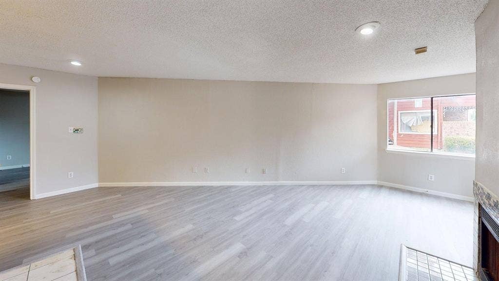 Open-concept space featuring wood-finish flooring, recessed lighting, a stone-surround fireplace, and a large multi-pane window