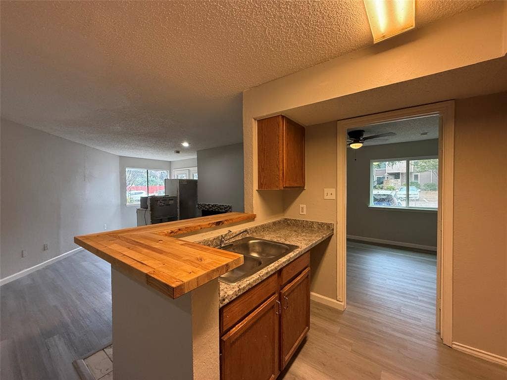 Kitchen featuring a butcher block breakfast bar, stone-patterned laminate countertops, dual-basin stainless steel sink, and wood-finish cabinetry
