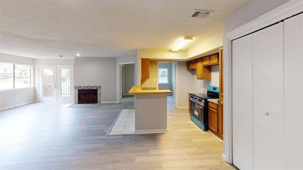 Open living area featuring wood-finish flooring, a stone-surround fireplace, dual glass-paneled exterior doors, a breakfast bar, and custom wood cabinetry