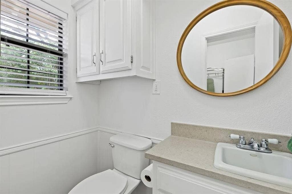 1101 N Waddill Street, McKinney, TX 75069 Vanity featuring a stone-surface countertop, white cabinetry, integrated sink with dual-handle faucet, oval mirror, and wall-mounted storage cabinet