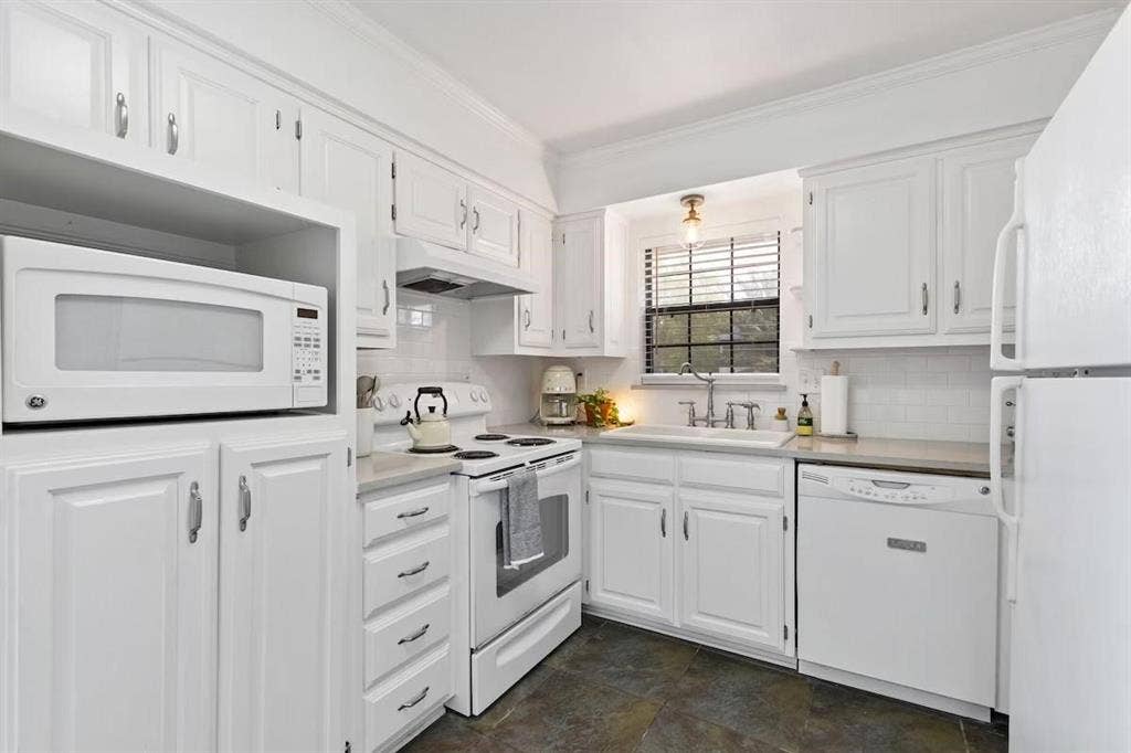1101 N Waddill Street, McKinney, TX 75069 Kitchen featuring white shaker-style cabinetry, tiled backsplash, stone-finish flooring, built-in microwave, and recessed faucet with a farmhouse-style sink