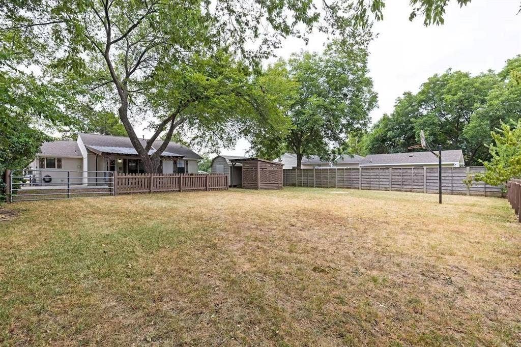 1101 N Waddill Street, McKinney, TX 75069 Expansive backyard featuring mature shade trees, a wooden perimeter fence, a detached storage structure, and an integrated basketball hoop