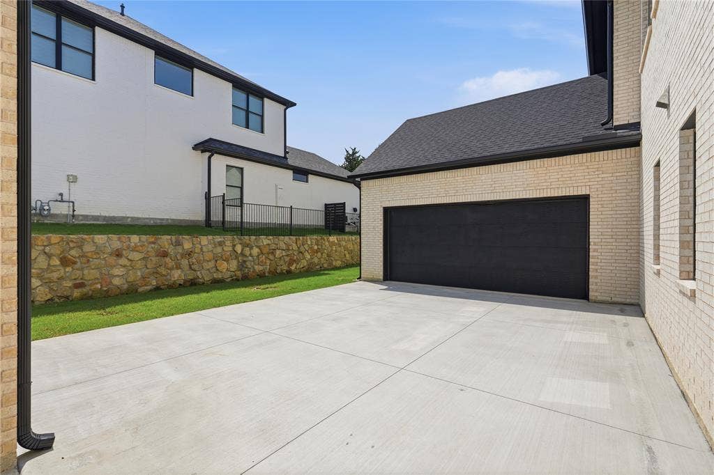 Spacious concrete driveway leading to a modern black garage door