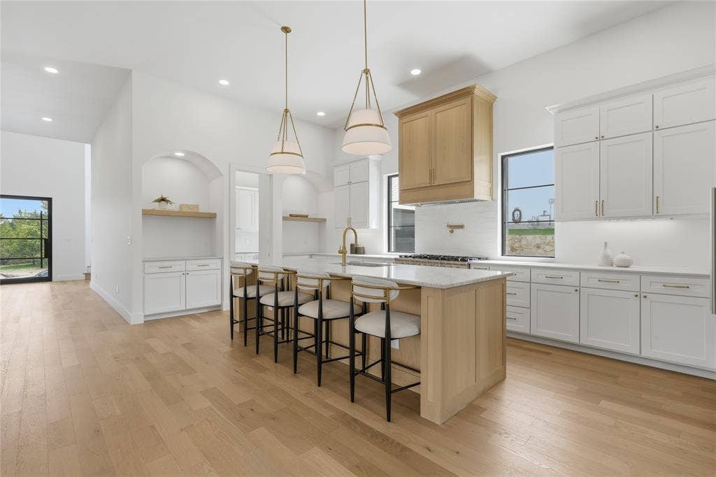 Kitchen featuring an expansive island with seating, pendant lighting, wood-finish flooring, white cabinetry, and stainless steel appliances