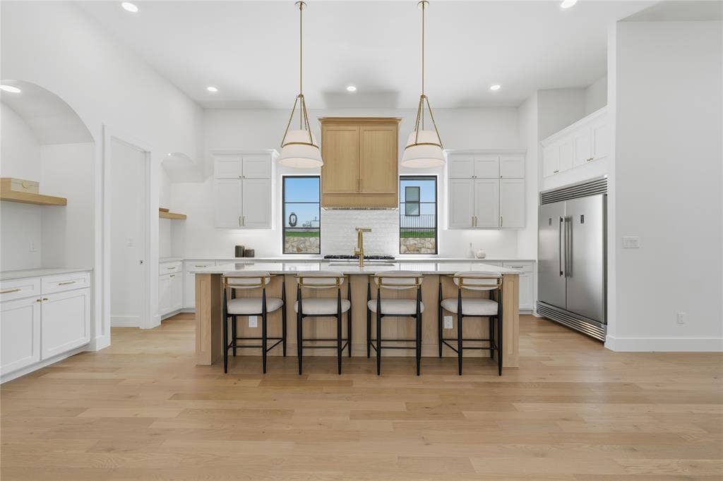 Gourmet kitchen featuring a central island with bar seating, stainless steel appliances, extensive white cabinetry, light wood-finish flooring, and two statement pendant lights