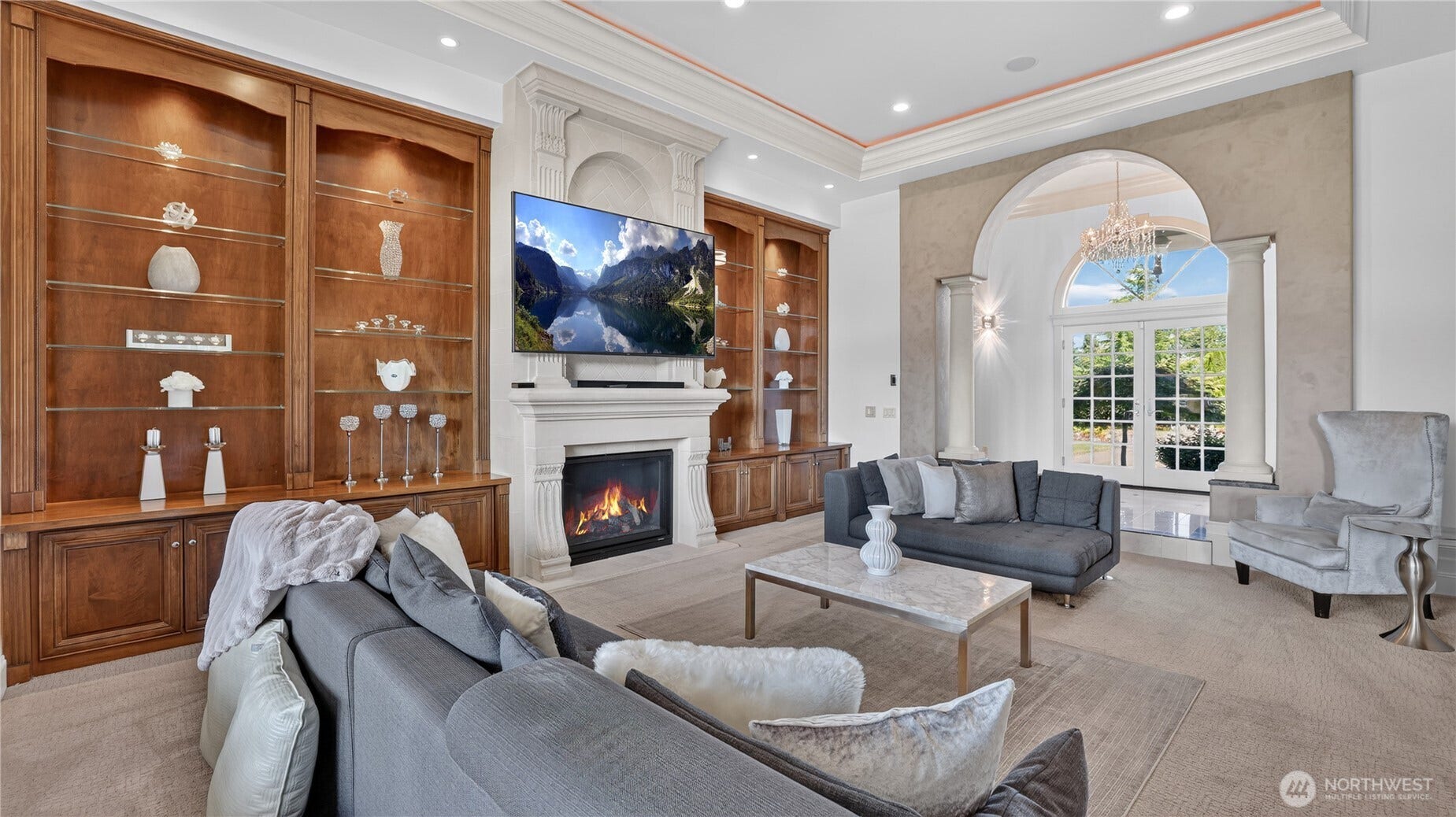Sunken Living Room    This elegant sunken living room exudes sophistication and warmth, featuring custom built-in wood cabinetry, a grand fireplace with detailed molding, and arched architectural accents that frame the space beautifully. The neutral palette and plush seating create a refined yet inviting atmosphere, while the high ceilings and recessed lighting enhance the sense of openness. Perfect for entertaining or relaxing by the fire, this room seamlessly blends luxury design with comfort.