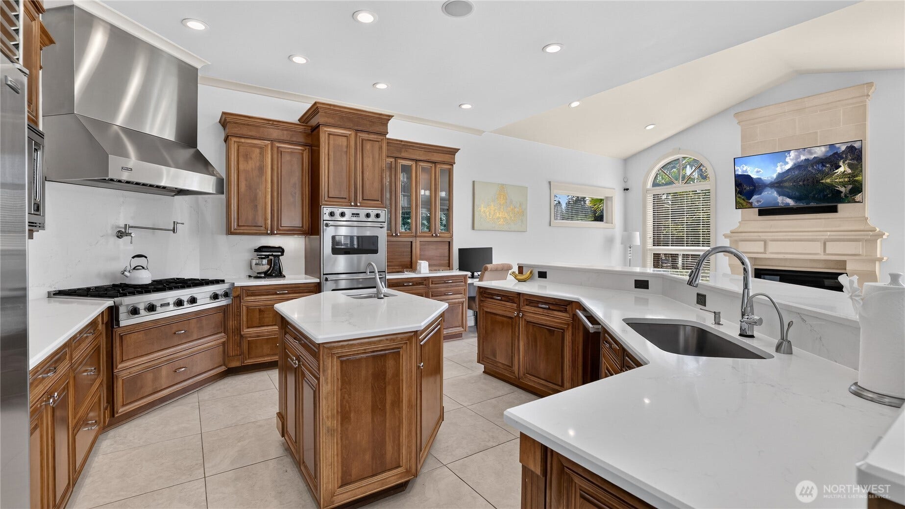 This impressive kitchen is designed for both culinary artistry and everyday luxury. Outfitted with professional-grade Viking appliances, it features a double oven, six-burner gas range, and built-in microwave, all complemented by a Sub-Zero refrigerator for optimal food preservation. A 120-bottle temperature-controlled wine refrigerator anchors the space, perfect for entertaining or fine dining at home. The layout includes a central prep island with sink, pot filler, and expansive workspace counters finished in sleek quartz. Rich wood cabinetry, stainless accents, and recessed lighting complete the sophisticated aesthetic, while the open flow to the adjacent living area ensures seamless connection between cooking and gathering spaces.