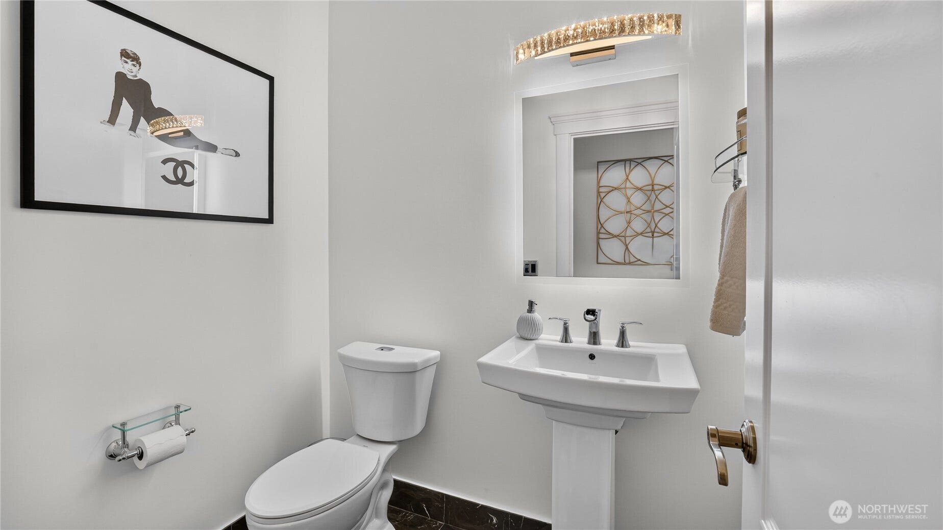 This chic powder bath combines modern simplicity with designer flair. Crisp white walls and a pedestal sink with polished chrome fixtures create a clean, timeless look, while the illuminated mirror and elegant light fixture add a touch of glamour. Dark marble flooring completes the space, offering a refined and sophisticated impression for gues