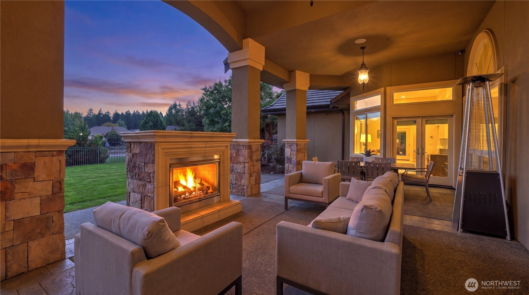 Outdoor Patio Retreat    This elegant covered patio offers the perfect blend of comfort and sophistication, featuring a stone-framed fireplace that creates a warm, inviting ambiance for evening gatherings. With plush seating, overhead lighting, and seamless indoor-outdoor flow, its an ideal space for relaxing or entertaining year-round. The open design frames serene views of the landscaped yard and sunset skies, elevating outdoor living to a luxurious experience.