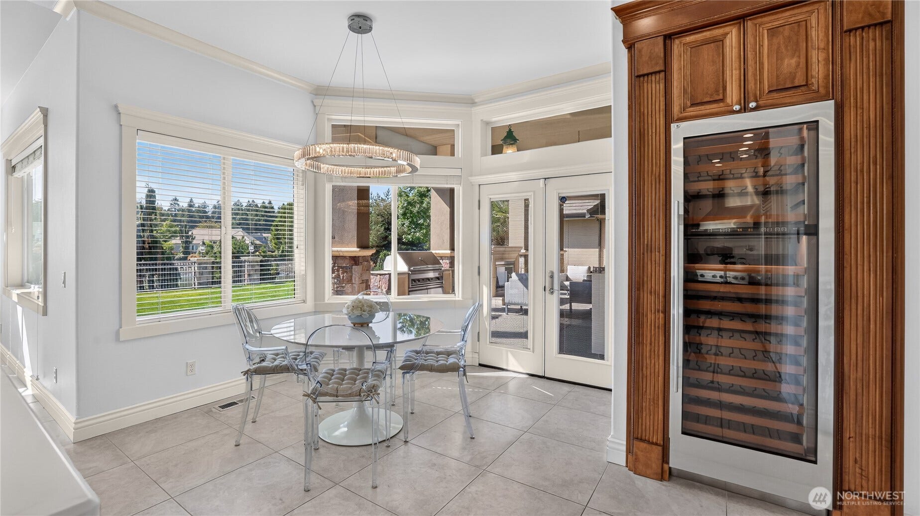 This bright and airy eating nook off the kitchen offers a seamless blend of style and functionality. Framed by large windows and French doors, the space is bathed in natural light and opens directly to the covered patio for effortless indoor-outdoor dining. A modern circular chandelier adds a touch of elegance above the glass-top table, while the built-in wine refrigeratorset within rich wood cabinetryprovides both convenience and sophistication. With polished tile flooring and crisp trim detailing, this nook is the perfect spot for casual meals or morning coffee overlooking the manicured grounds.