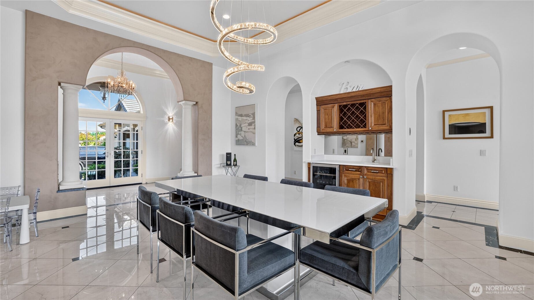 Formal Luxury Dining Room    This breathtaking formal dining room blends architectural grandeur with modern sophistication. Framed by arched columns and soaring ceilings, the space is anchored by a striking sculptural chandelier that adds a contemporary flourish. Polished marble floors and elegant wall finishes create a refined backdrop for gatherings, while natural light pours through the arched French doors, highlighting the seamless flow to adjoining living spaces. A perfect setting for elegant entertaining and memorable occasions.
