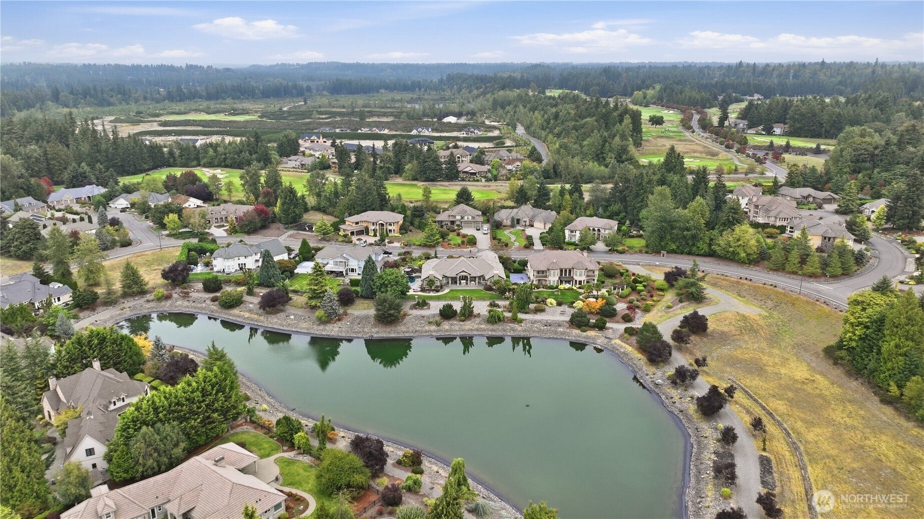 Neighborhood and Setting    This aerial view showcases the propertys prime location within an exclusive lakeside community, surrounded by lush greenery and manicured landscapes. The subject home sits prominently along the waters edge, offering serene views and a beautifully maintained yard. The neighborhood features spacious estates, winding streets, and natural scenery, all framed by forested hills and nearby golf course fairways. A perfect blend of elegance and tranquility, this setting highlights the areas prestige and peaceful charm.
