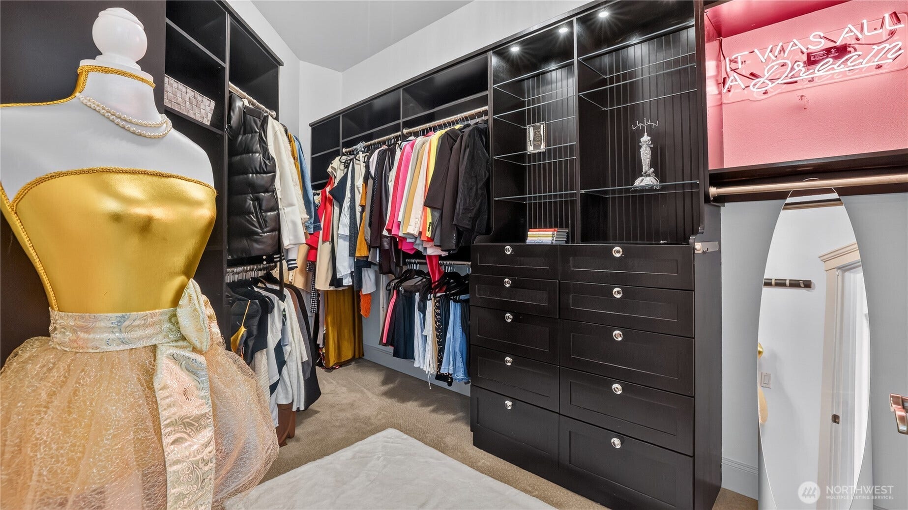 Primary Suite Closet    This sophisticated walk-in closet offers exceptional organization and style, featuring custom dark wood cabinetry, built-in drawers, and open shelving with accent lighting. Thoughtfully designed for functionality and elegance, it provides ample space for wardrobe storage and display, creating a polished extension of the primary suite.