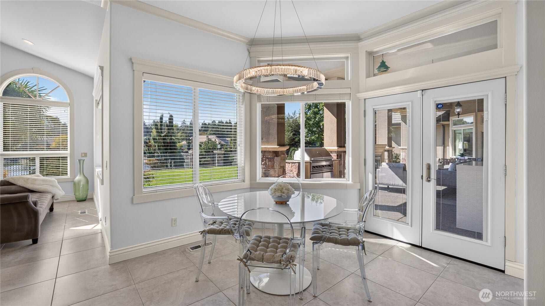 Eating Nook off Kitchen    This bright and inviting eating nook offers a seamless connection between indoor comfort and outdoor living. Framed by large picture windows and French doors, the space is filled with natural light and overlooks the lush backyard and patio. A modern chandelier adds a touch of elegance above the dining table, while neutral tones and tile flooring create a clean, sophisticated atmosphereperfect for casual meals or morning coffee with a view.