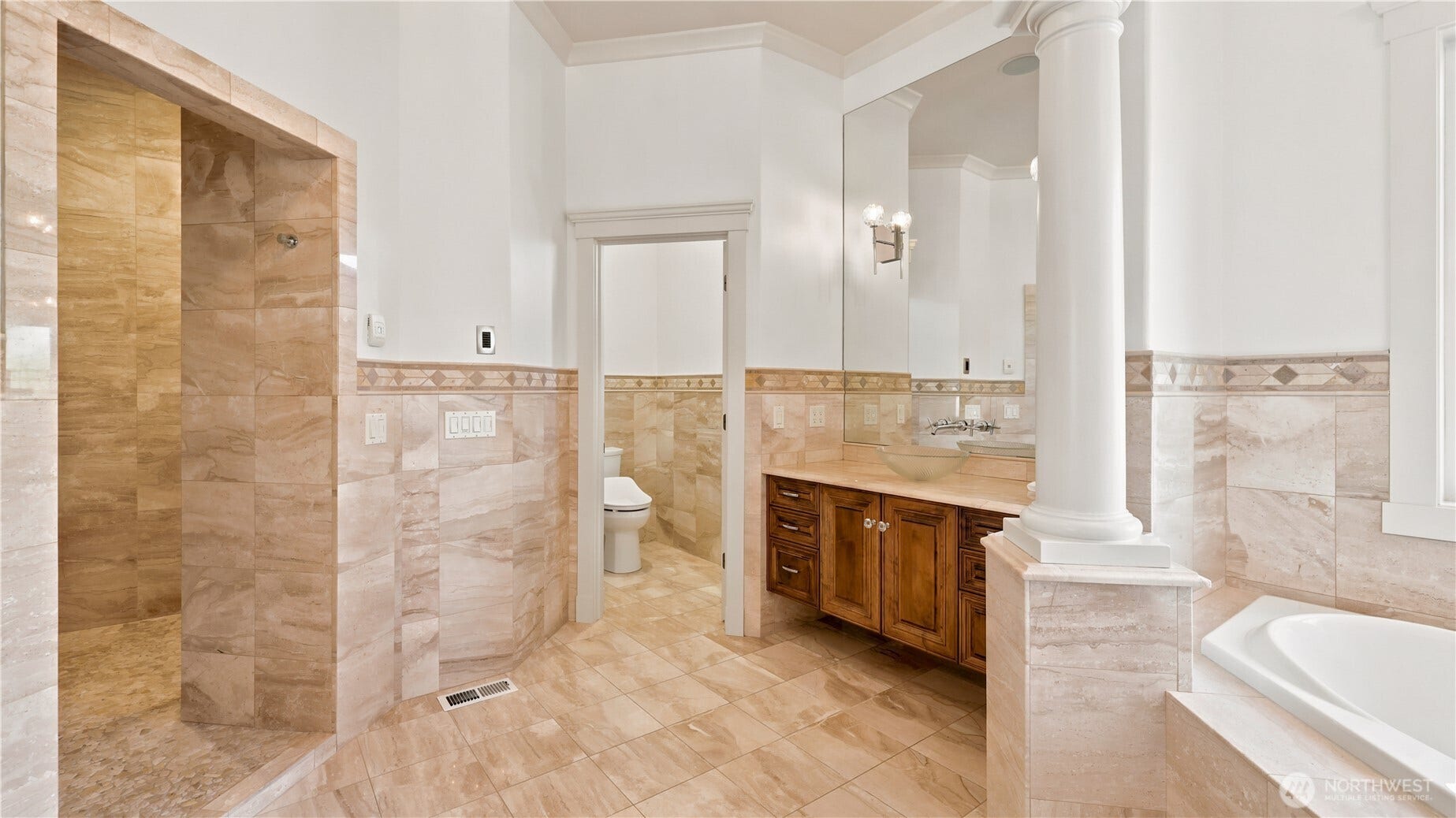 Primary Suite Bathroom    This luxurious primary bathroom showcases timeless elegance with warm marble tile, architectural columns, and a spacious walk-in shower. The design blends classic craftsmanship with modern comfort, featuring a deep soaking tub, custom wood vanity, and refined lighting. Thoughtfully appointed for relaxation and style, it offers a serene retreat that complements the sophistication of the primary suite.