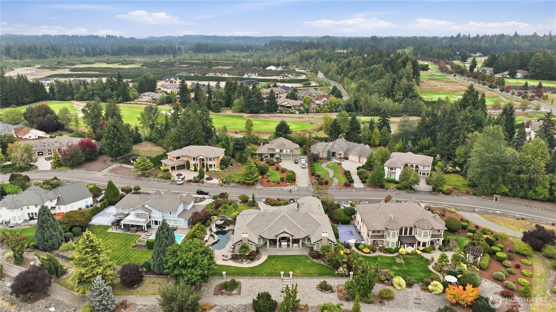 Neighborhood Overview    This aerial view highlights the stunning community setting, with the subject property prominently centered among beautifully maintained estates. The neighborhood features lush landscaping, manicured lawns, and tree-lined streets, offering a serene and picturesque environment. Beyond the homes, the backdrop reveals rolling golf course fairways and forested hills, creating a harmonious blend of luxury living and natural beauty. The location provides both privacy and scenic views, making it an exceptional place to call home.