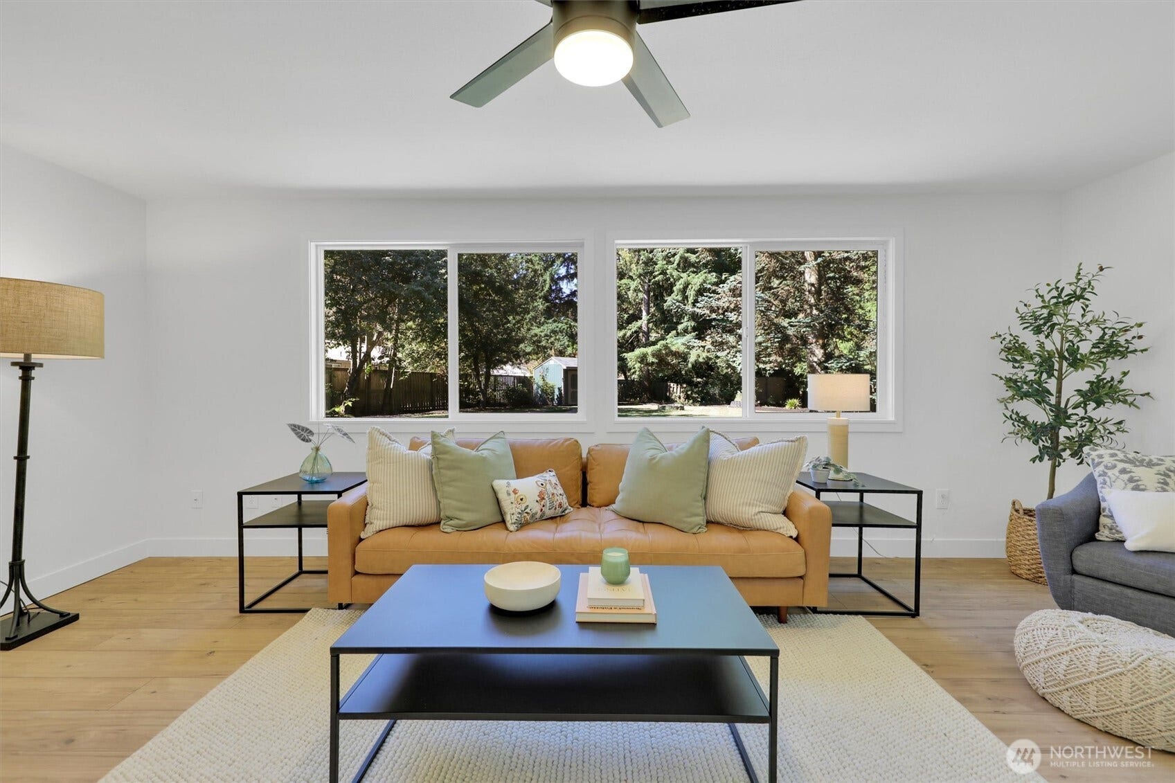 20915 W Richmond Road, Bothell, WA 98021 Bright living room centered around a sofa and coffee table with large picture windows, ceiling fan, and views of mature trees.
