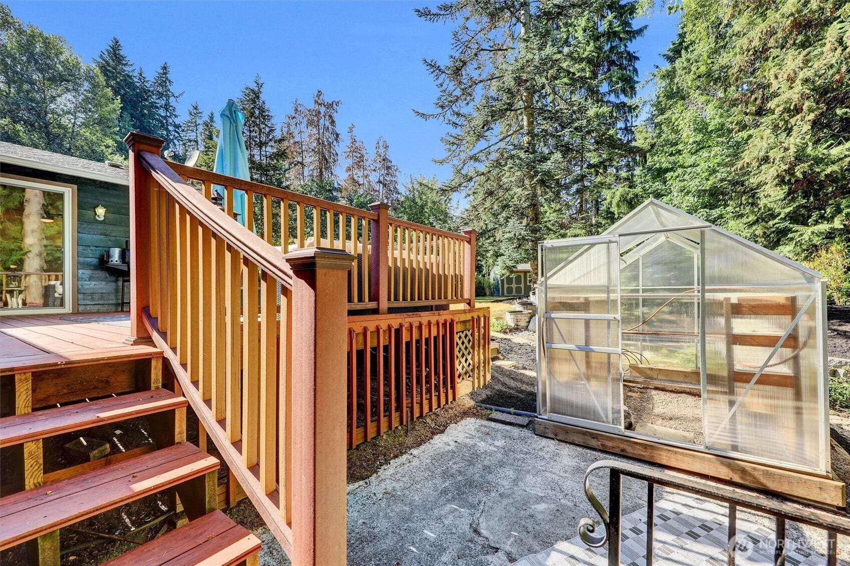 20915 W Richmond Road, Bothell, WA 98021 Rear outdoor area featuring a raised wood deck, stairs, railing, greenhouse, and mature trees surrounding the property.